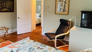 A room with a wooden floor, a black chair, a white desk, and a bed in the background.