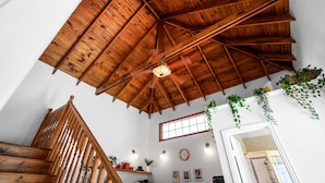 Une pièce spacieuse avec un haut plafond en bois, un escalier en bois et une grande fenêtre.
