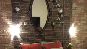 A bedroom with a brick wall, a large mirror, a bed with red and beige bedding, and two bedside tables with small plants. - Casa Cielo (Valle de Bravo)