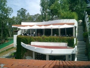 A modern building with a curved roof, large windows, and outdoor seating under white umbrellas.