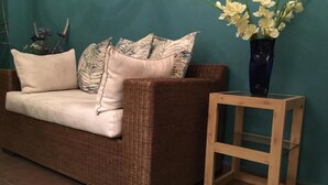 A wicker sofa with cushions, a wooden side table with a vase of flowers, and a teal wall. - Casa Cielo (Valle de Bravo)