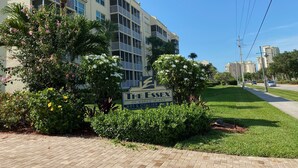 A multi-story residential building with balconies, surrounded by lush greenery and flowering plants.
