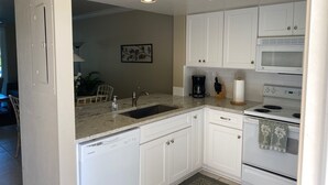 A kitchen with white cabinets, a dishwasher, a sink, a coffee maker, a microwave, and an oven.