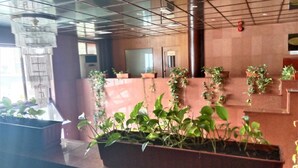 A modern interior with a large planter filled with green plants, a glass partition, and a wooden reception desk. - Al Commodore Hotel (Manama)