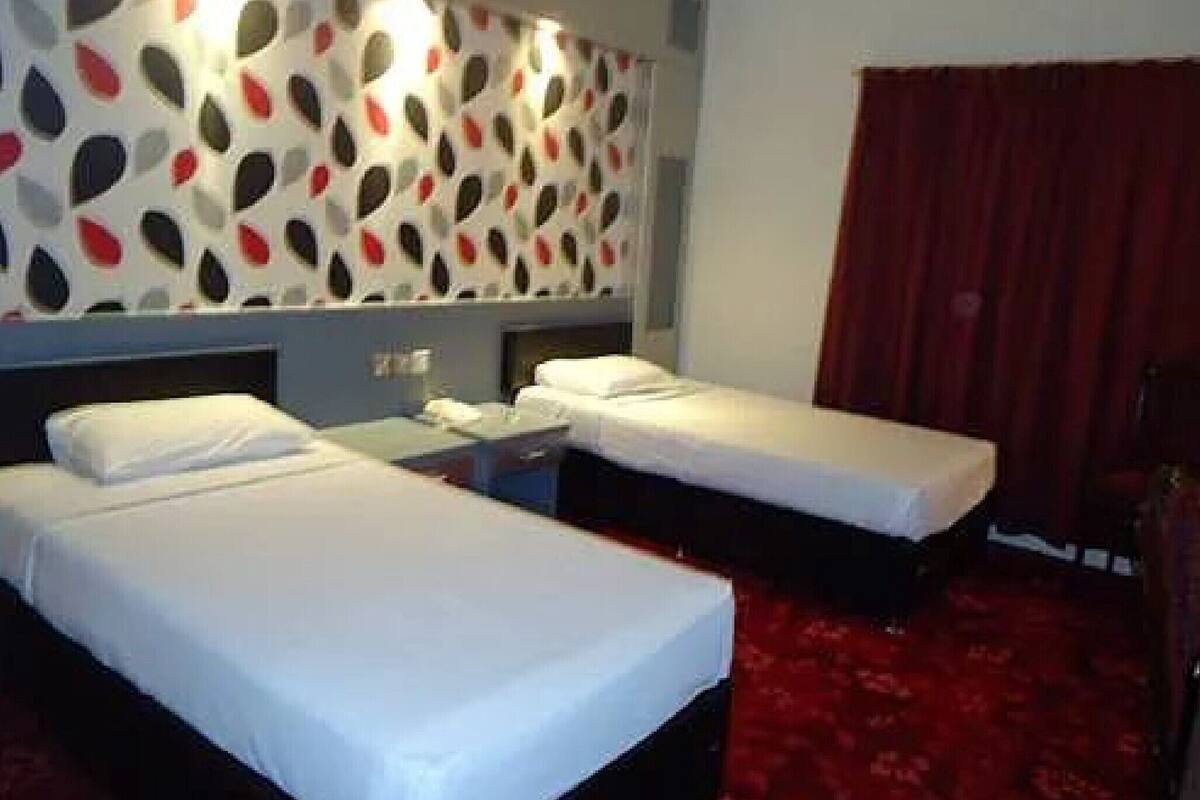 Une chambre d'hôtel avec deux lits simples, un mur à motifs et une moquette rouge.