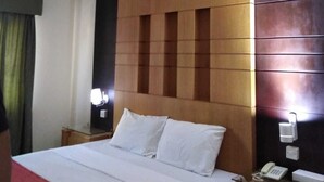 A hotel room with a large bed, a wooden headboard, a bedside table with a lamp, and a telephone. - Al Commodore Hotel (Manama)