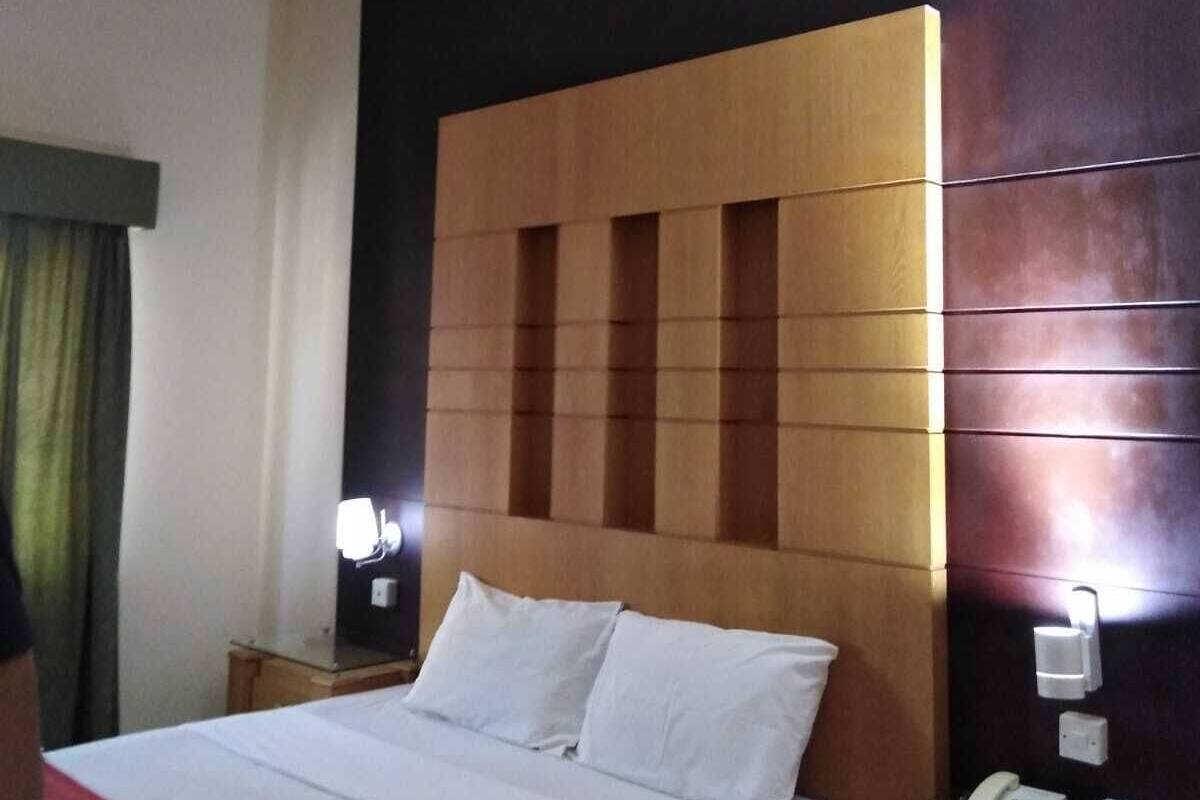 Une chambre d’hôtel avec un grand lit, une tête de lit en bois, une table de chevet avec une lampe et un téléphone.