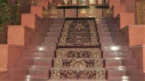 A grand staircase with ornate carpeted steps leading to a landing with framed pictures. - Al Commodore Hotel (Manama)