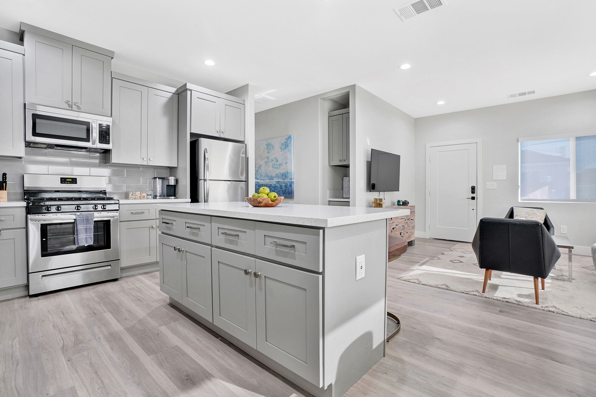 A modern kitchen with stainless steel appliances, grey cabinetry, and a central island with a bowl of fruit.