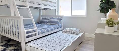 A bunk bed with a ladder, a window with blinds, a potted plant, and a small table.