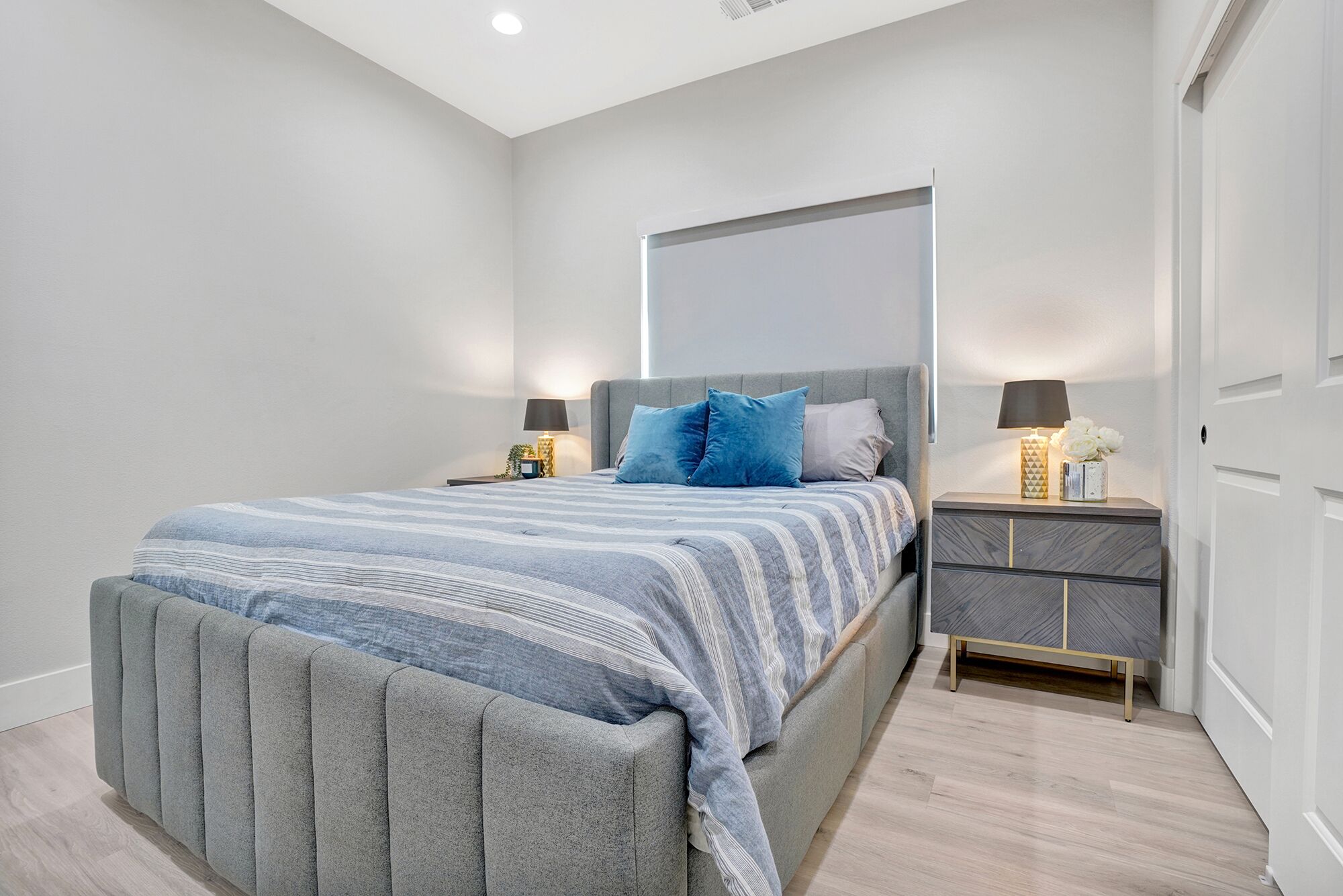 Een moderne slaapkamer met een groot bed, twee nachtkastjes met lampen en een kledingkast.