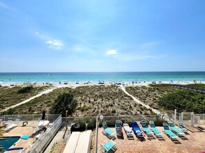 Une vue sur la plage avec une piscine, des chaises longues et un ciel dégagé.