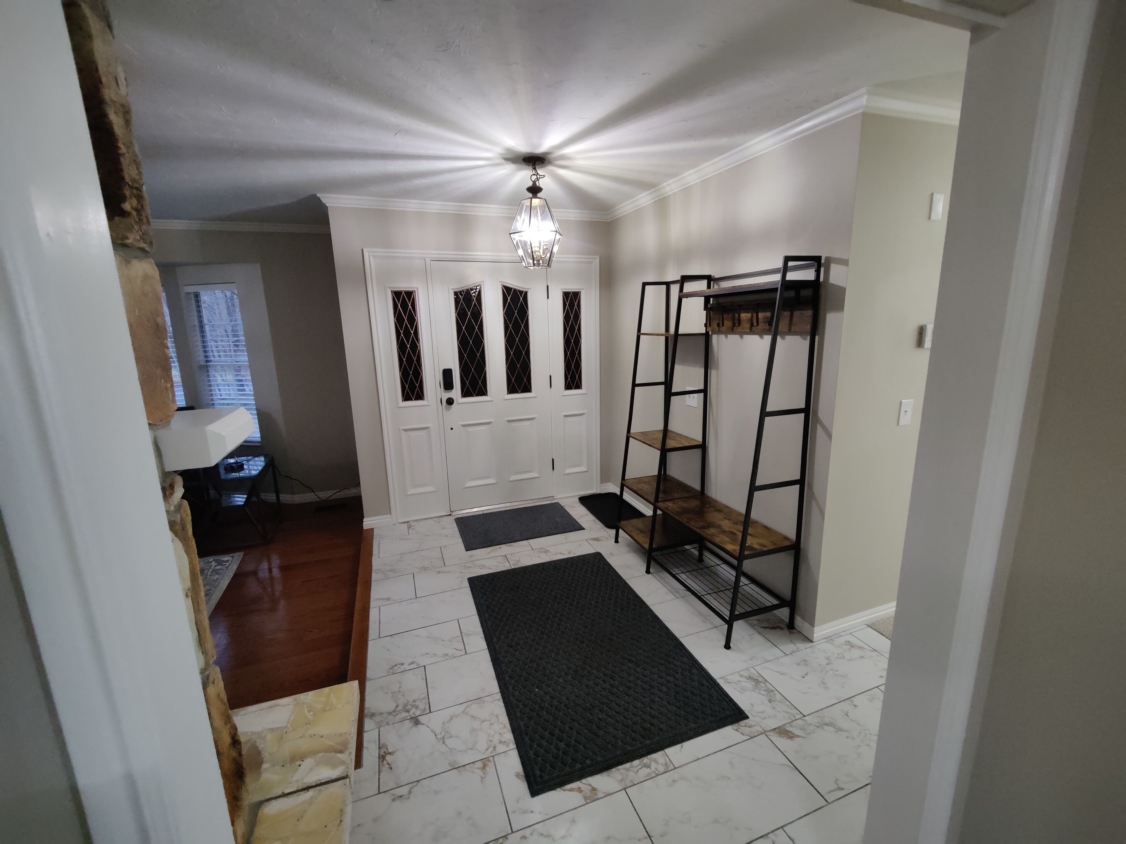 A hallway with a white door, a black metal shelf unit, and a black rug.