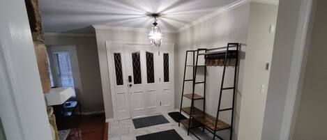 A hallway with a white door, a black metal shelf unit, and a black rug.