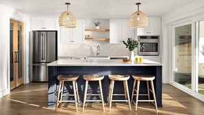 Een moderne keuken met een groot eiland, roestvrijstalen apparatuur en houten krukken.
