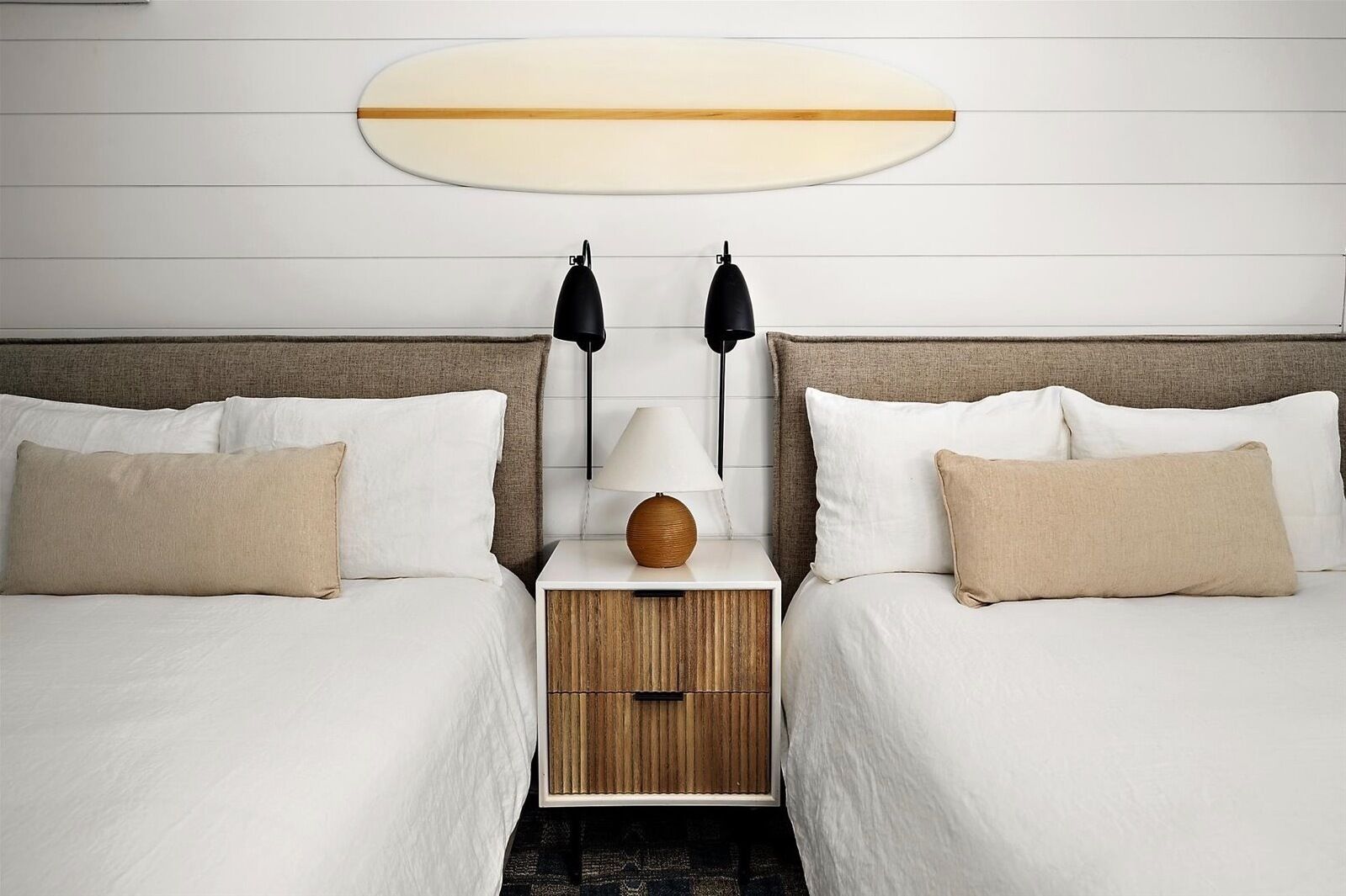 Een hotelkamer met twee bedden, een nachtkastje, een lamp en een surfplank aan de muur.