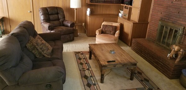 A cozy living room with a dark brown leather armchair, a beige armchair, a wooden coffee table, and a fireplace.