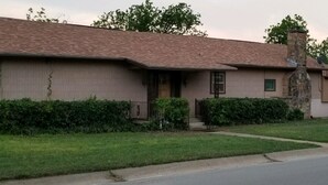 A single-story house with a brick exterior, a stone chimney, and a front porch.