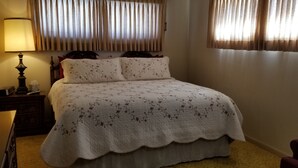 A neatly made bed with a floral bedspread, a bedside lamp, and a wooden nightstand with a radio.