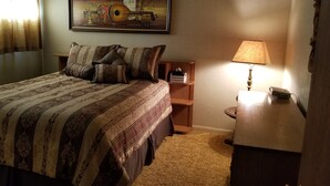 A neatly made bed with patterned bedding, a bedside table with a lamp, and a small shelf with a tissue box.