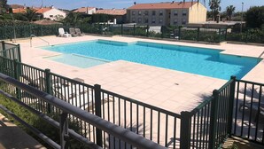 Una piscina rectangular con solárium alicatado, rodeada por una valla metálica verde.
