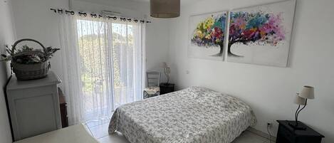 Une chambre à coucher avec un lit, un bureau, une chaise, une lampe, une fenêtre avec des rideaux et un tableau au mur.