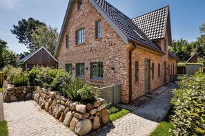 A traditional brick house with a stone pathway leading to the entrance, surrounded by greenery.