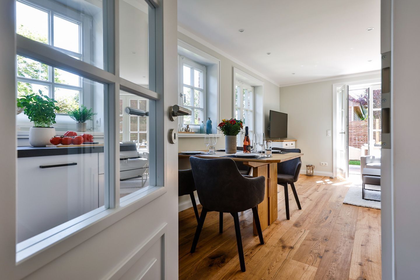 A modern kitchen with a dining area, wooden flooring, and large windows.