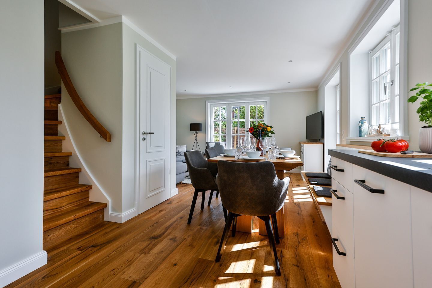 A modern kitchen with wooden flooring, white cabinetry, and a dining area with chairs and a table.