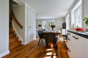 Een moderne keuken met houten vloeren, witte kasten en een eethoek met stoelen en een tafel.