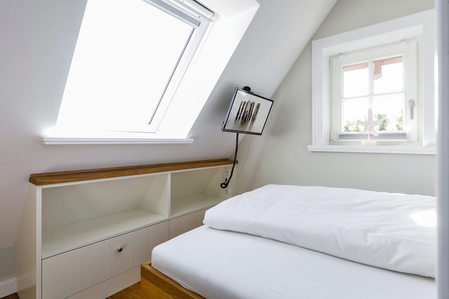 A bedroom with a skylight, a bed, a bedside table, and a window.