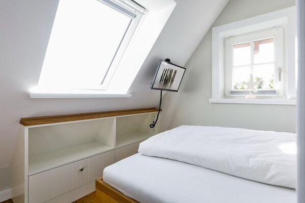 A bedroom with a skylight, a bed, a bedside table, and a window.