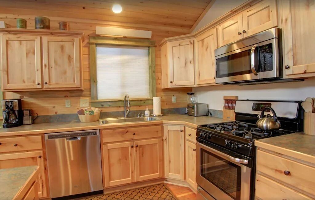A kitchen with wooden cabinets, stainless steel appliances, a dishwasher, and a window with blinds.