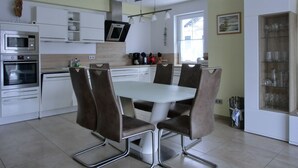 A modern kitchen with white cabinets, stainless steel appliances, and a dining area with a white table and brown chairs. - Vacation apartment LP7 "Seestern" - 3-room apartment (approx. 92 m²) for 5 persons - on the 2nd floor in (Graal-Müritz)