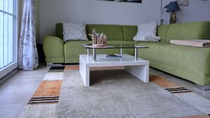 A living room with a green sofa, a glass coffee table, and a window with curtains. - Vacation apartment LP7 "Seestern" - 3-room apartment (approx. 92 m²) for 5 persons - on the 2nd floor in (Graal-Müritz)