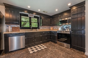 A modern kitchen with dark cabinets, stainless steel appliances, and a checkered rug.