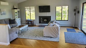 Ein großzügiges Wohnzimmer mit Kamin, einem großen an der Wand befestigten Fernseher und einer gemütlichen Sitzecke mit Sofa und Couchen.