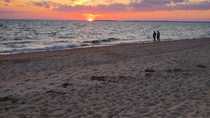 Ein Strand bei Sonnenuntergang, zwei Personen spazieren, ruhige See.