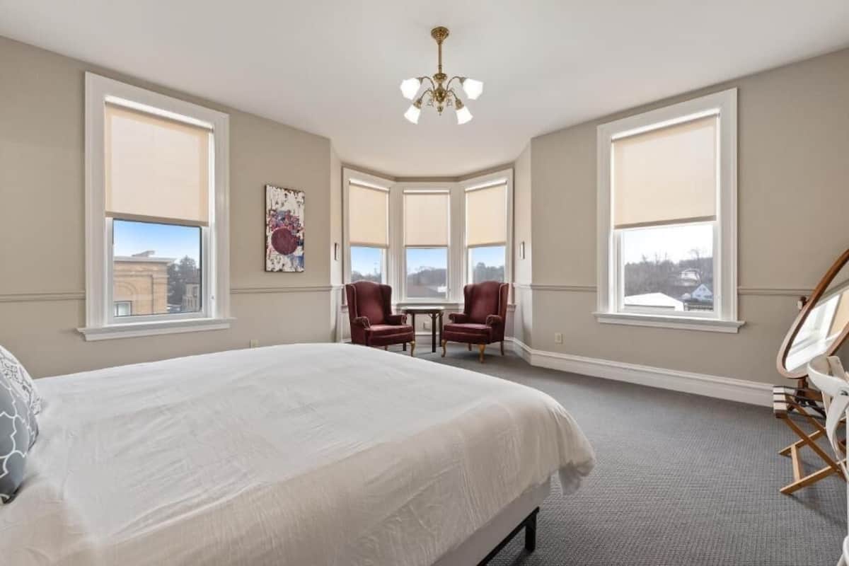 A bedroom with a large bed, two armchairs, a small table, and a mirror.