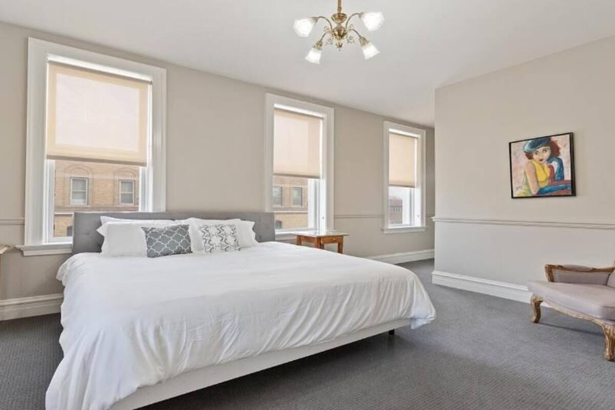 A bedroom with a large bed, two bedside tables, a chair, and a painting on the wall.