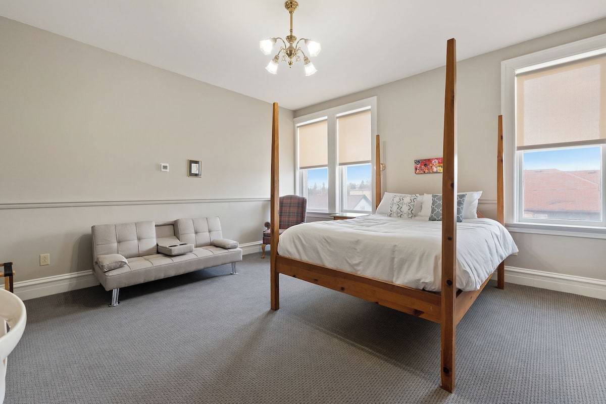 A bedroom with a four-poster bed, a sofa, and large windows.