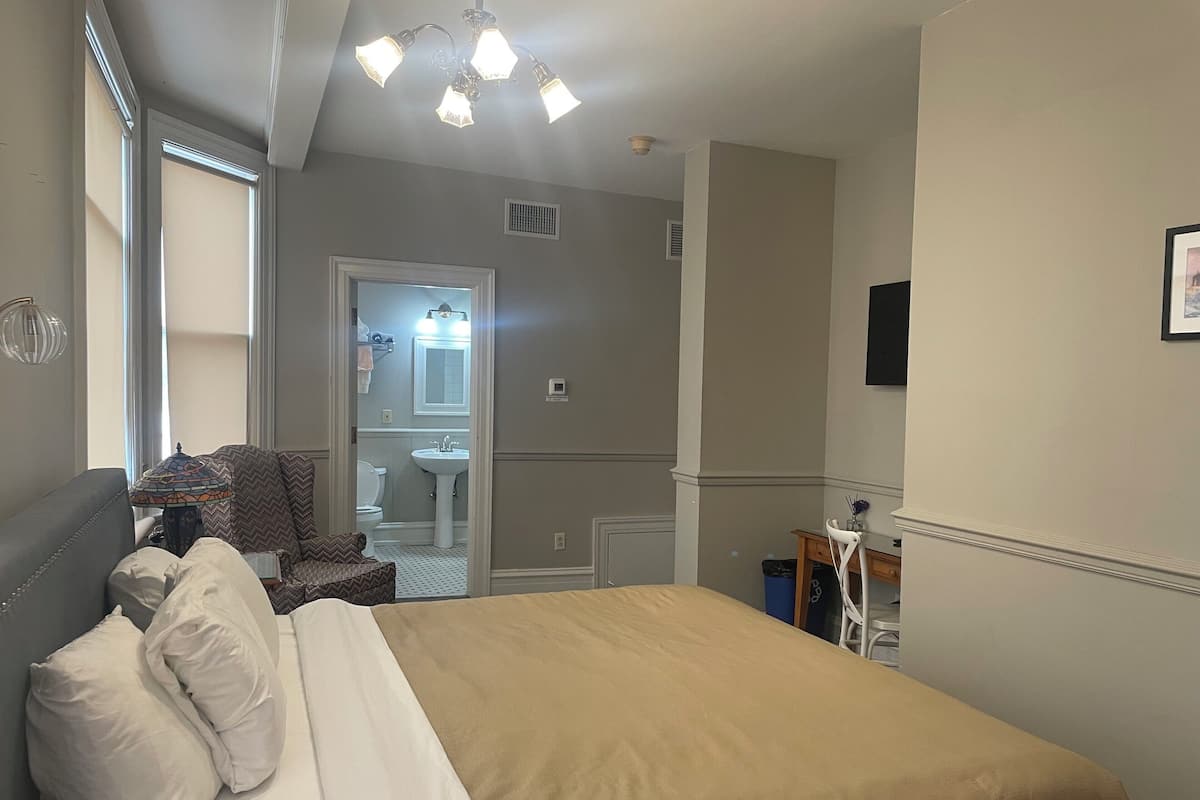 A bedroom with a bed, a chair, a desk, and a bathroom visible through an open door.