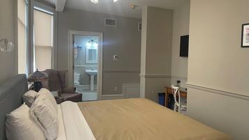 A bedroom with a bed, a chair, a desk, and a bathroom visible through an open door.