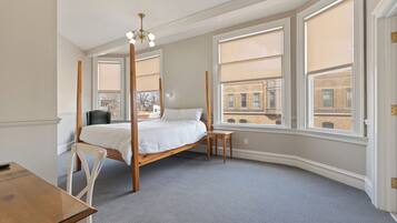 Un dormitorio con cama con dosel, un escritorio y ventanas amplias con vistas a la ciudad.