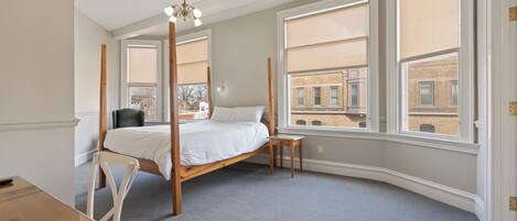 A bedroom with a four-poster bed, a desk, and large windows with city views.