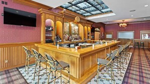 A bar area with a wooden bar, multiple stools, a large screen, and a glass ceiling.