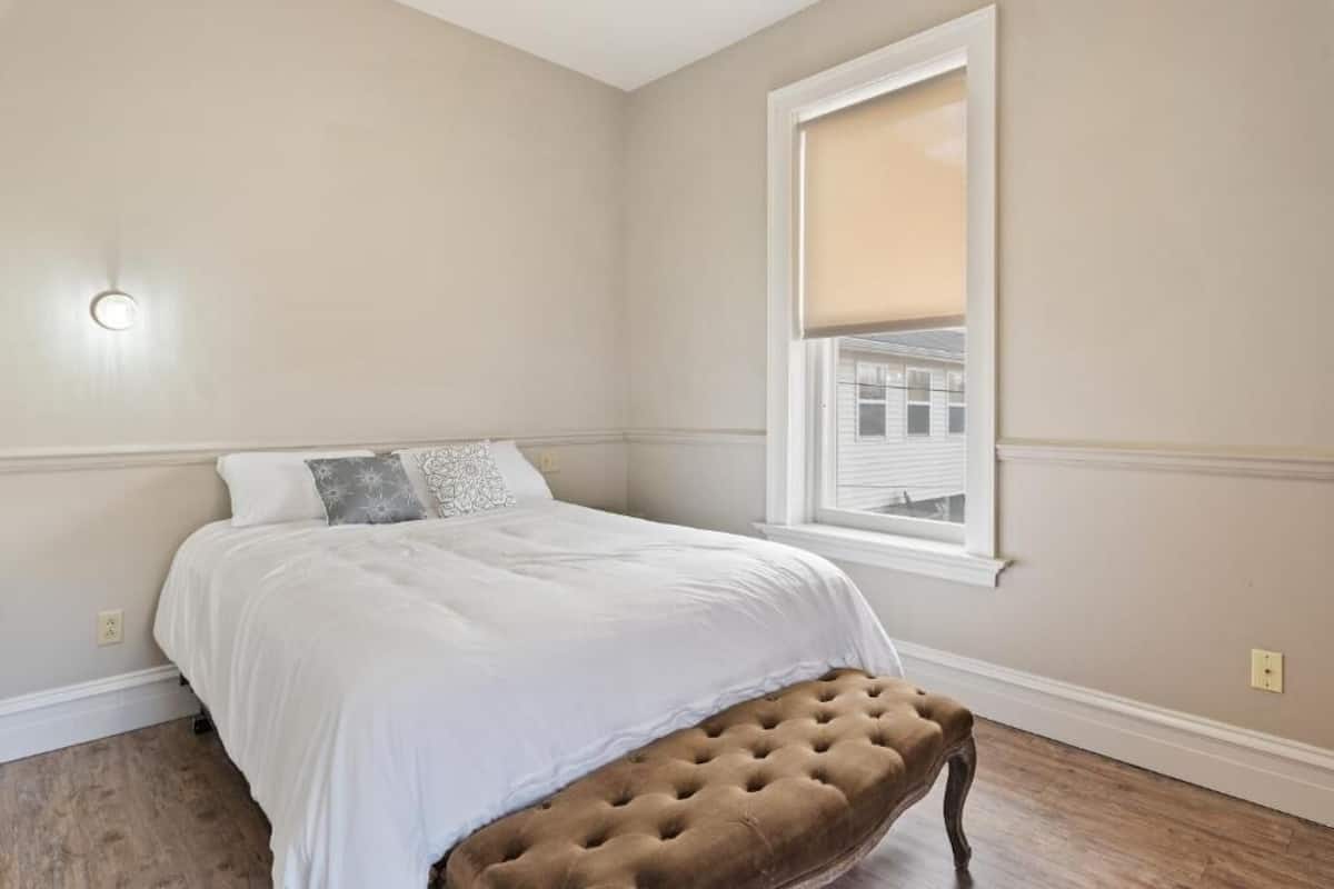 A bedroom with a bed, a window with blinds, and a wall-mounted light fixture.