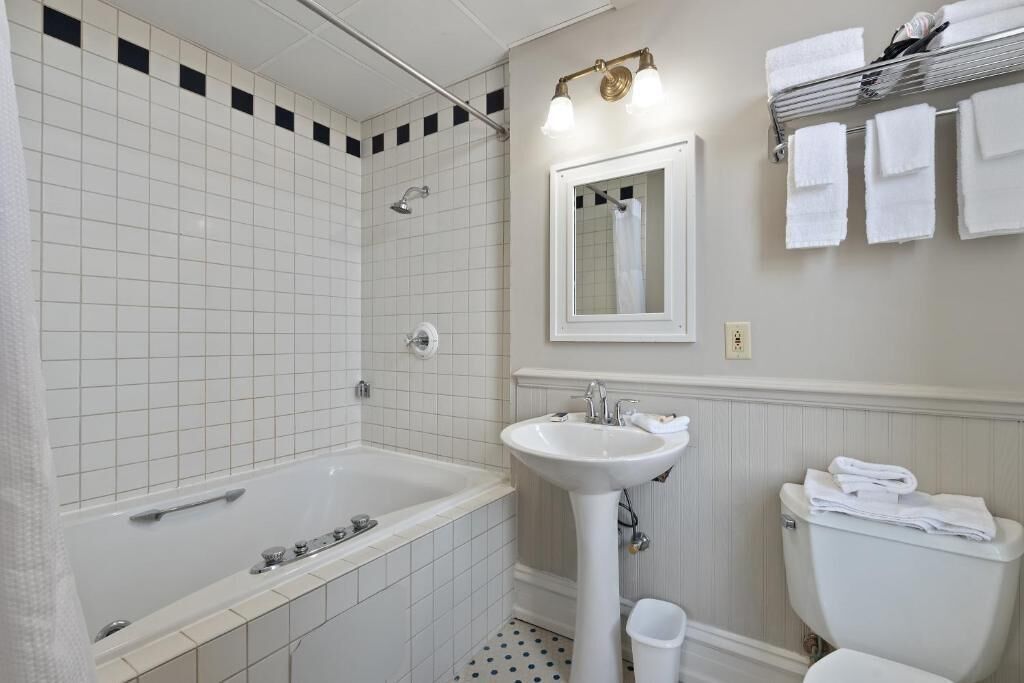 Une salle de bain avec une baignoire, un lavabo et des toilettes. Il y a un porte-serviettes au-dessus des toilettes et un miroir au-dessus du lavabo.