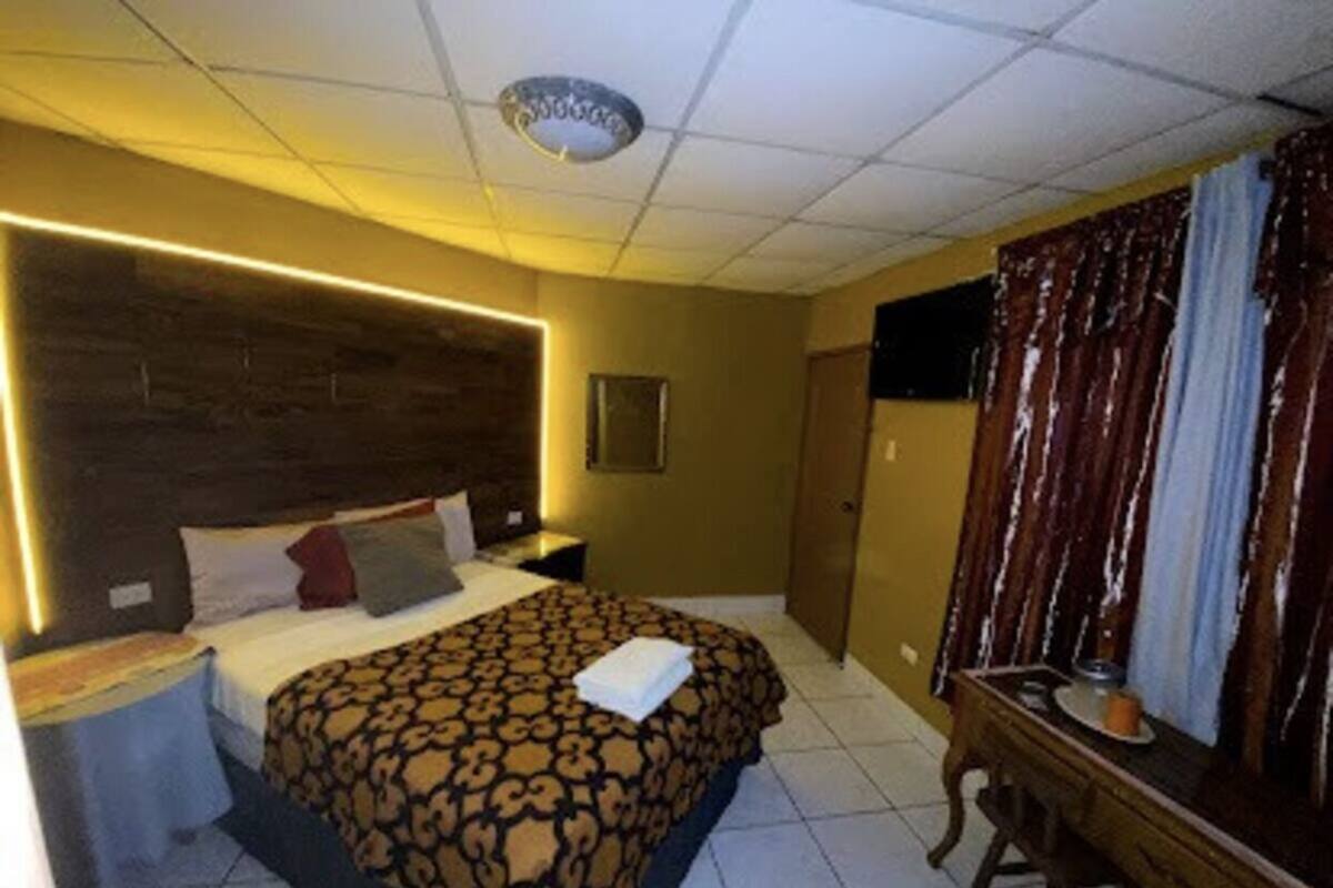 Quarto de hotel com uma cama grande, uma escrivaninha de madeira, uma mesa de cabeceira e um espelho.