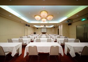 A conference room with rows of tables and chairs, a projector screen, and a chandelier.